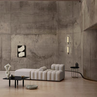 Modern beige sectional sofa against a grey concrete wall, complemented by black accents and minimalist decor.
