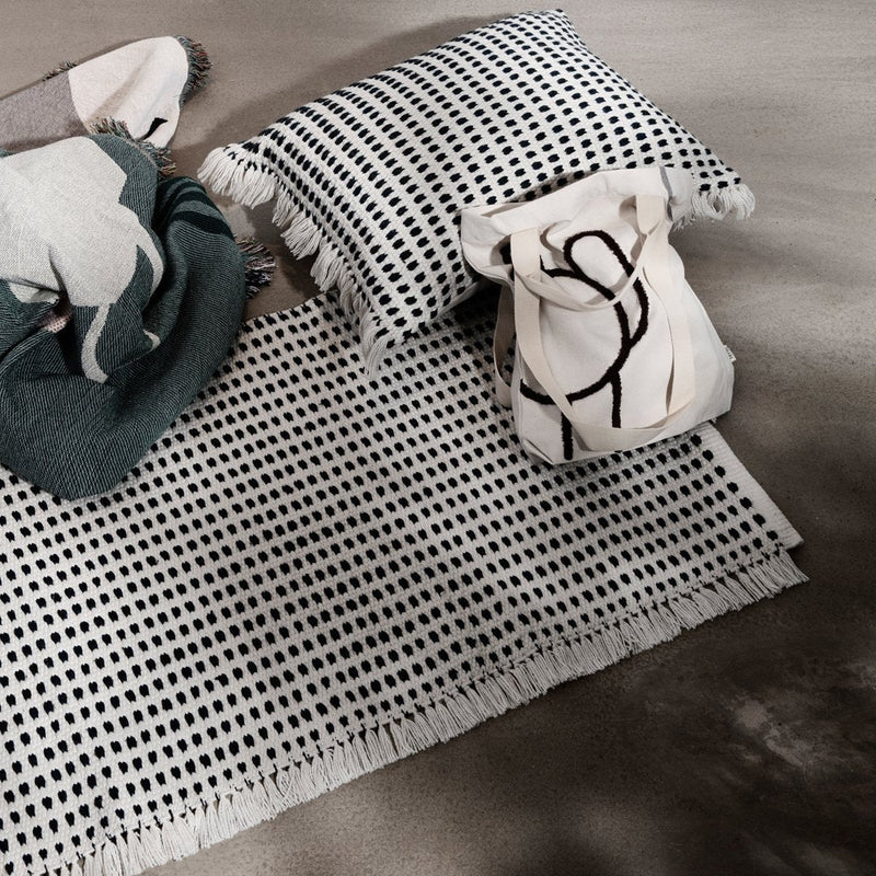 Black and white patterned rug with fringe, decorative pillow, and bag in a cozy, textured layout.