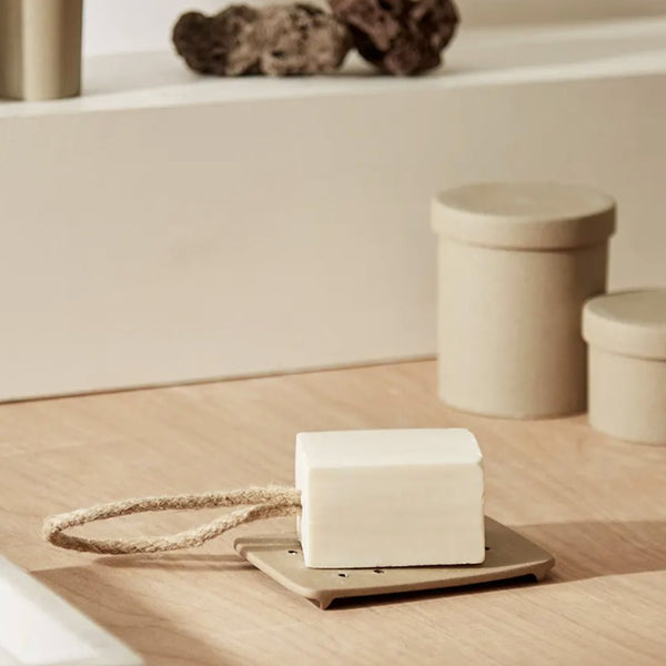 Minimalist white soap on a beige dish, surrounded by neutral-toned decor and natural textures.
