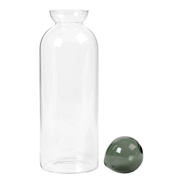 Clear glass bottle with a smooth surface and a glossy, dark green decorative orb nearby. Simple and elegant design.
