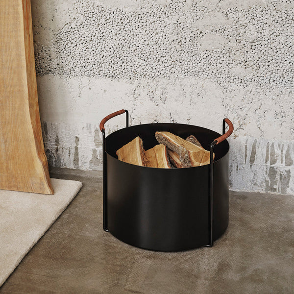 Stylish black metal log holder with tan leather handles, featuring a smooth, minimalist design.