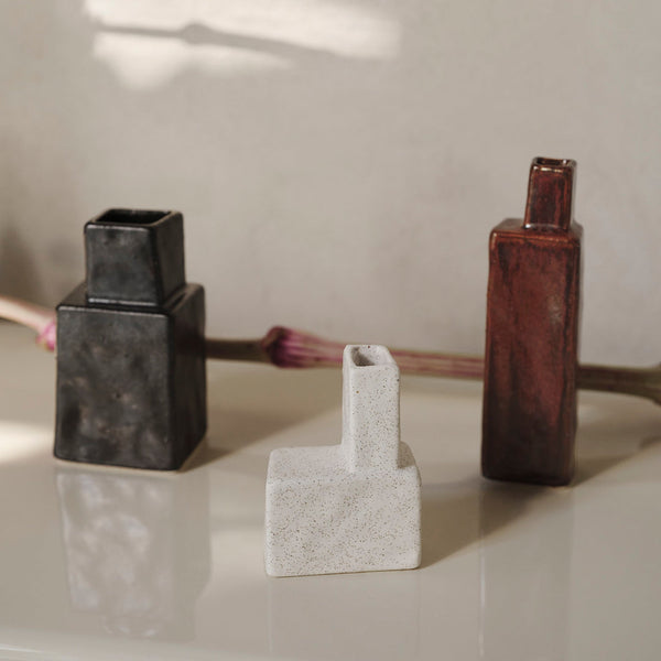Three modern vases: matte black, textured white, and glossy brown; geometric shapes complementing each other.