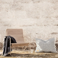 "Neutral beige chair with a textured black and white polka dot pillow against a rustic wall backdrop."