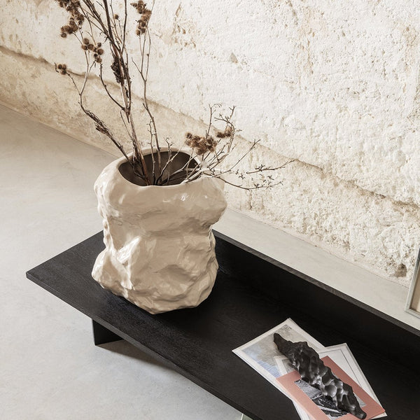 Textured beige vase with dried branches on a sleek black table, set against a neutral wall. Perfect for modern decor.