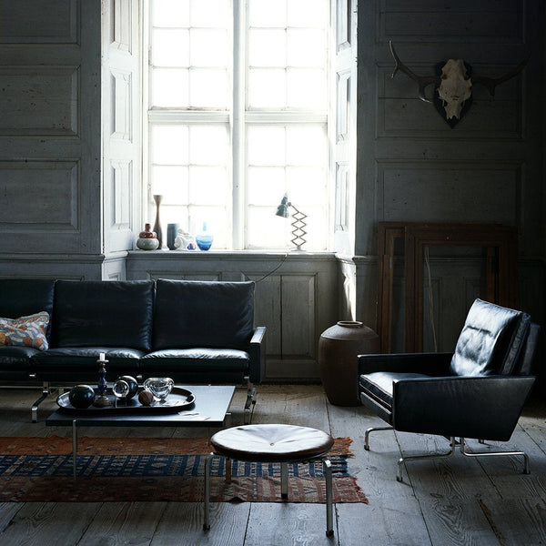 "Modern living room with black leather furniture, a dark patterned rug, and a light wood coffee table against gray walls."