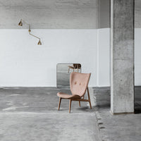 Blush pink upholstered chair with a tufted pattern on a minimalist gray concrete floor and white wall backdrop.