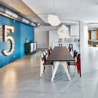 Modern dining space featuring a blue wall, wooden table, and colorful chairs with red and white accents.