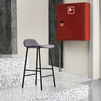 Gray upholstered bar stool with a sleek black frame on a speckled white terrazzo floor, accented by a red cabinet.
