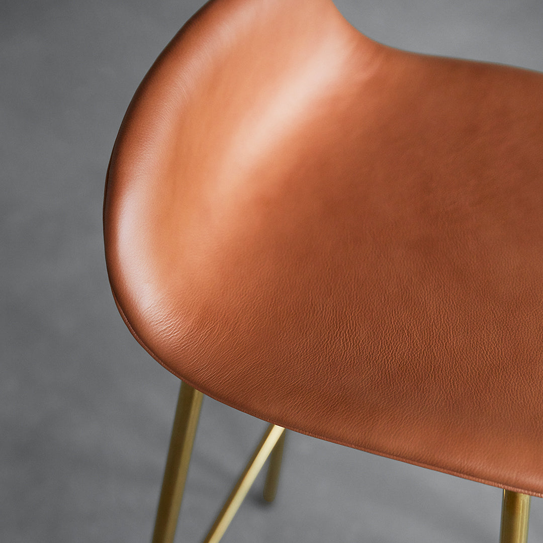 Brown leather chair seat with a smooth texture and gold metal legs against a gray background.