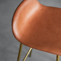 Brown leather chair seat with a smooth texture and gold metal legs against a gray background.
