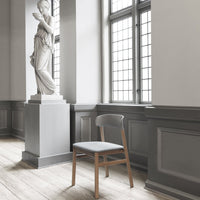 Gray chair with a smooth fabric seat, natural wood legs in a bright, modern space with neutral tones and large windows.