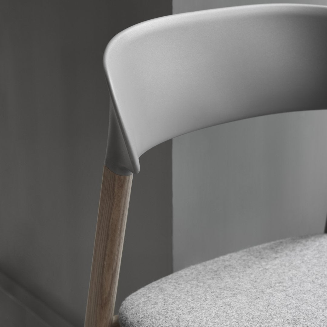 Gray chair with a smooth plastic back, wooden legs, and a textured gray fabric seat against a muted background.