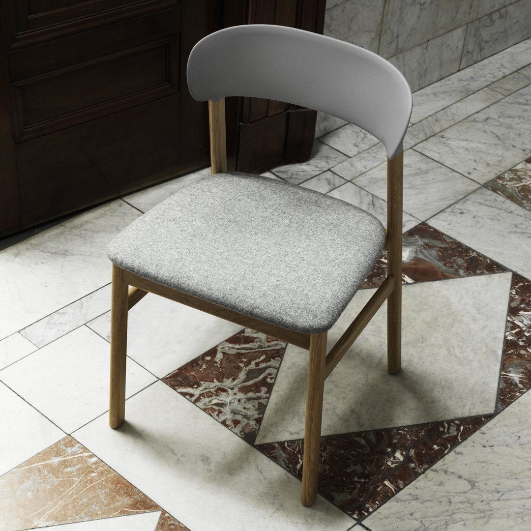 Gray upholstered chair with a curved white backrest on a patterned marble floor. Elegant and modern design.