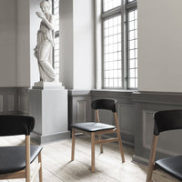 Black chairs with wooden legs on light wood flooring, set against grey walls and large windows. Minimalist and modern design.