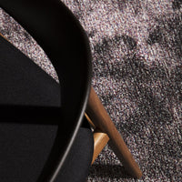 Black chair on textured gray and beige pattern rug, showcasing contrasting colors and intricate designs.