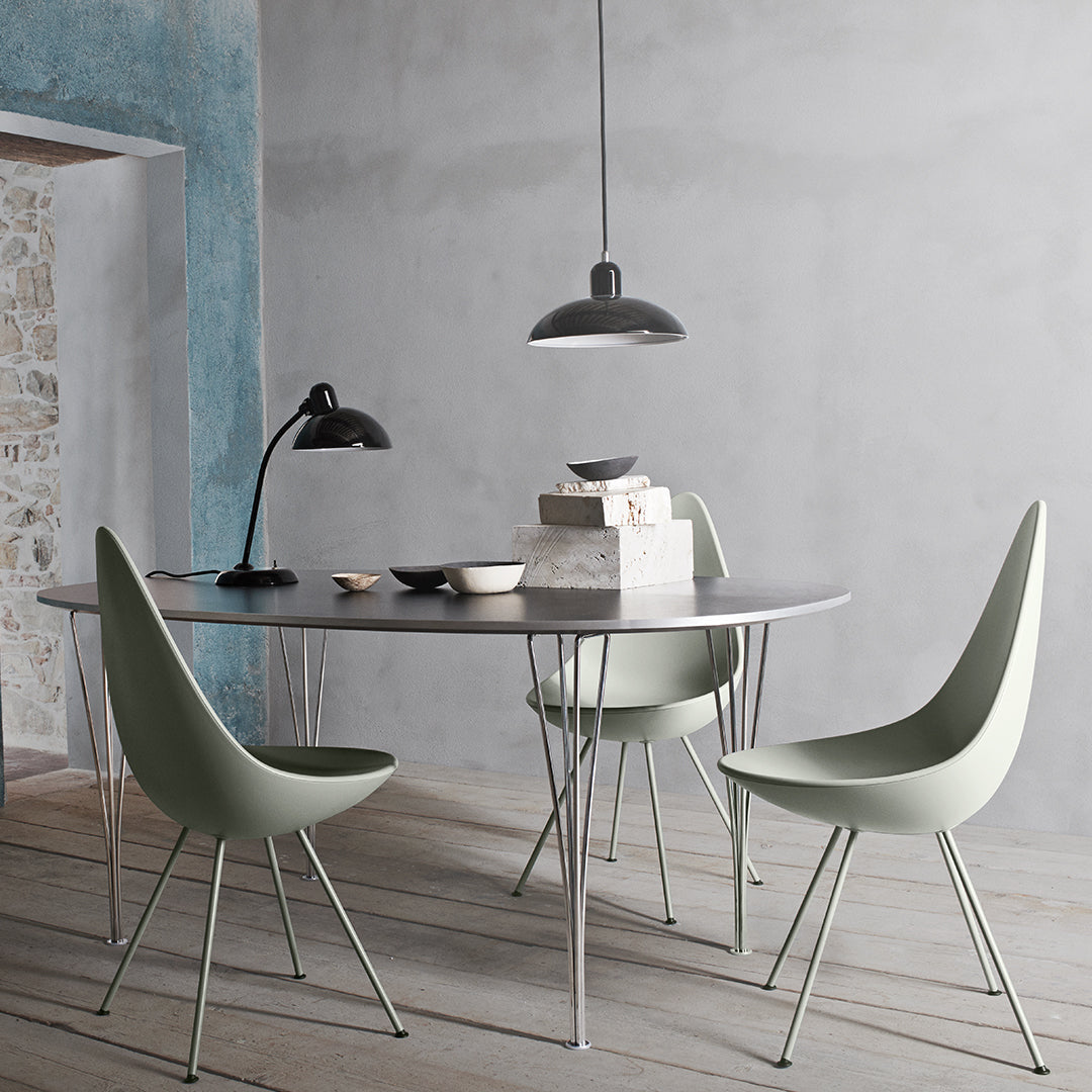 Modern dining setup featuring gray table, mint green chairs, and black pendant light against textured blue wall.