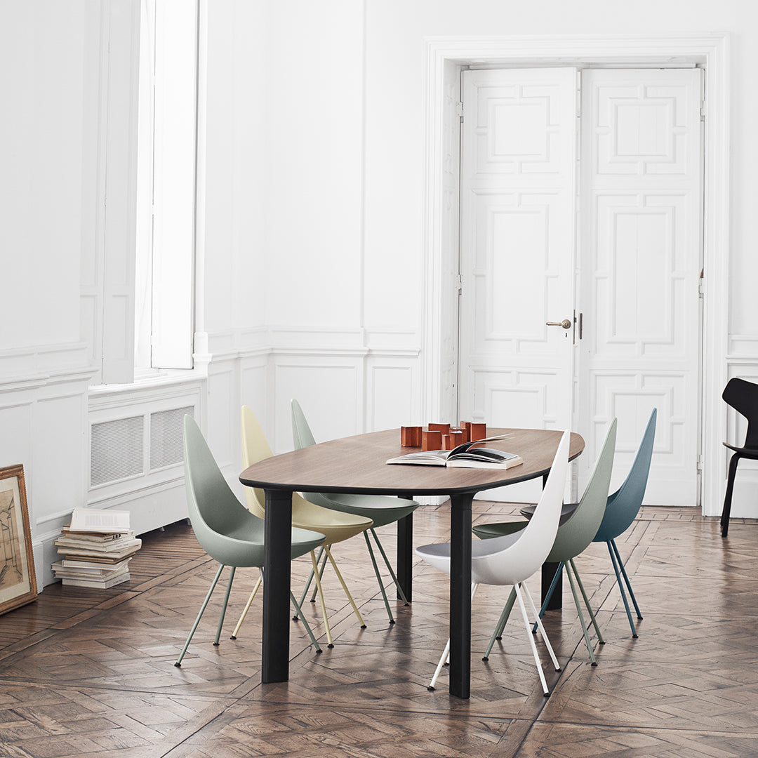 Modern wooden dining table with pastel-colored chairs in soft shades of green, blue, and yellow against a minimalist backdrop.
