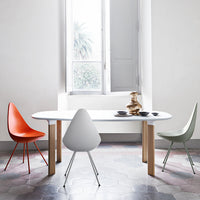 Modern table with white surface and wooden legs, surrounded by orange, white, and green chairs on patterned floor tiles.