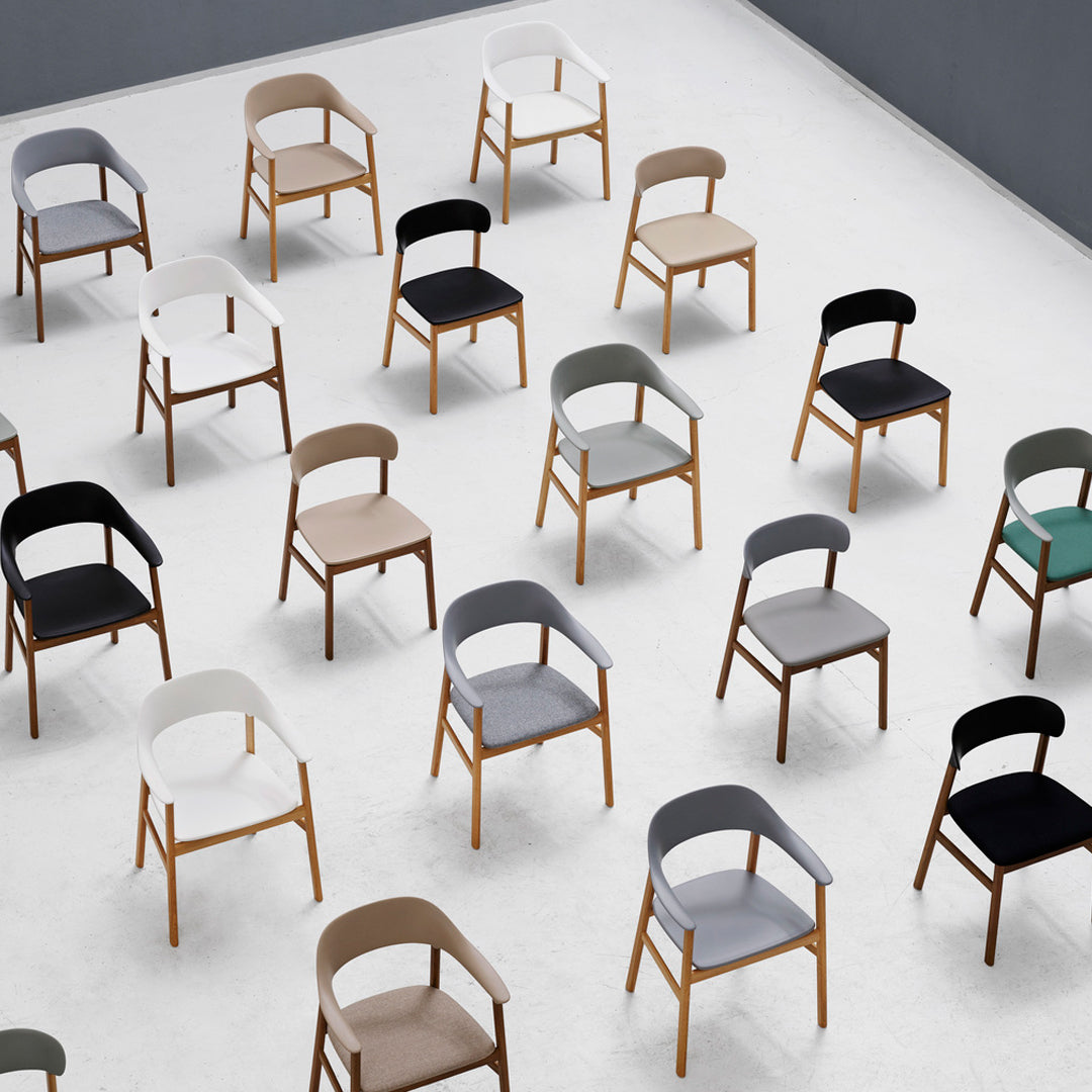 Colorful array of modern chairs in black, white, gray, beige, and green with wooden legs on a light floor.
