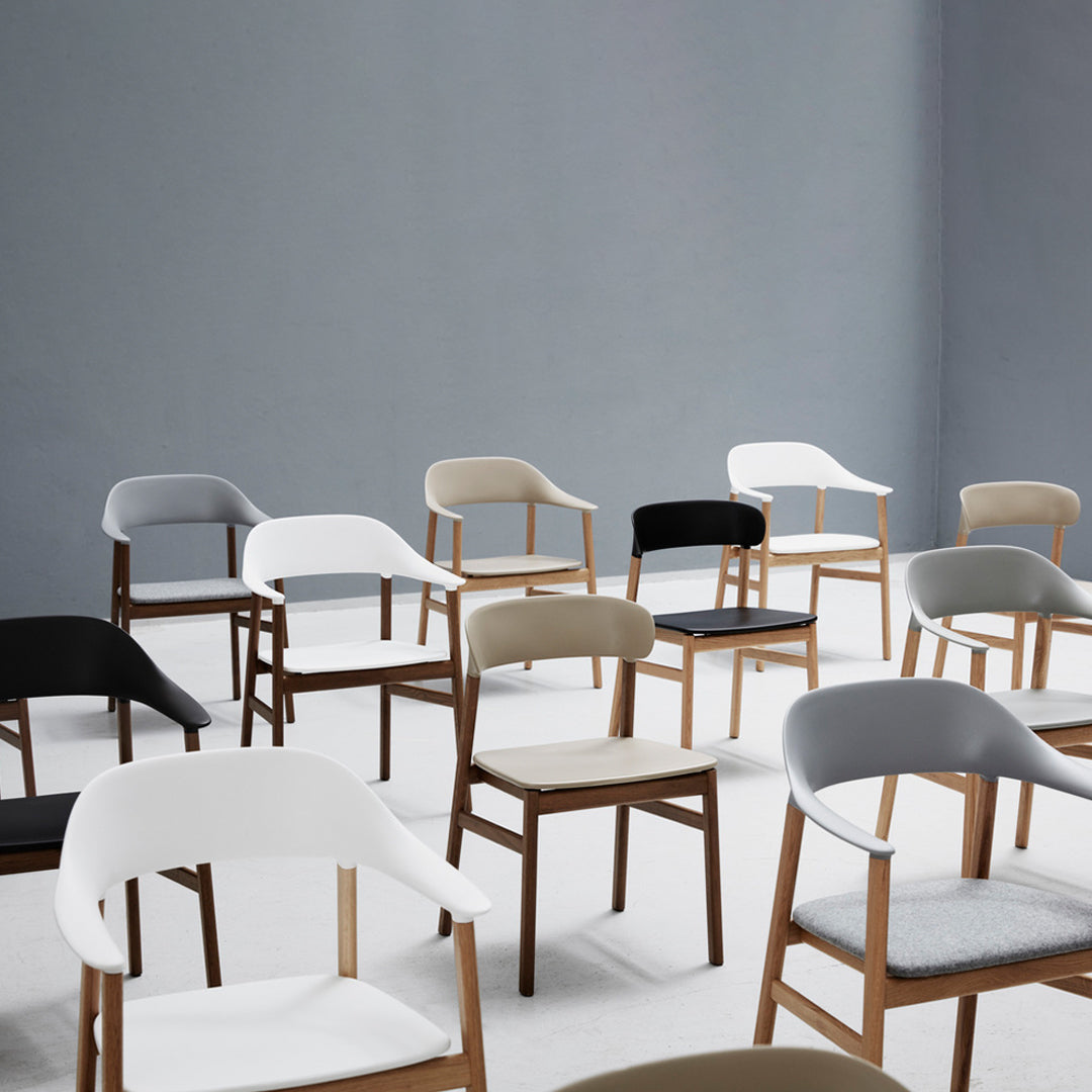 Variety of modern chairs in black, white, gray, and beige with sleek wooden legs, arranged against a light gray background.