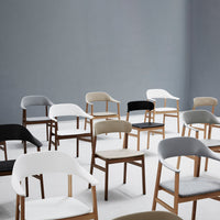 Variety of modern chairs in black, white, gray, and beige with sleek wooden legs, arranged against a light gray background.