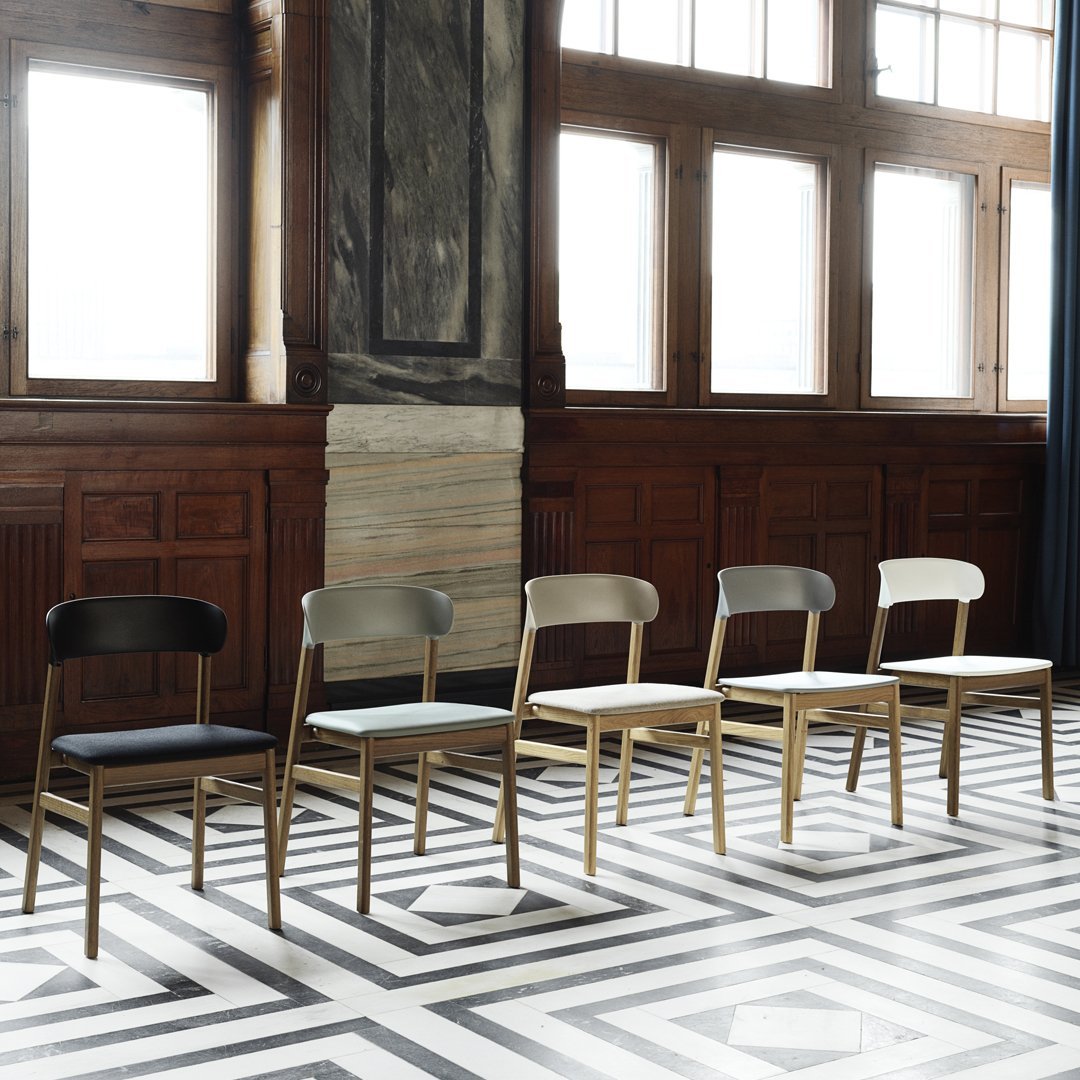 Five minimalist chairs in black, gray, white, and natural wood, set against a bold black and white geometric floor pattern.