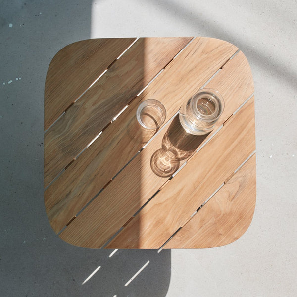 Light wood square table with natural slats, featuring glassware casting soft shadows in sunlight.