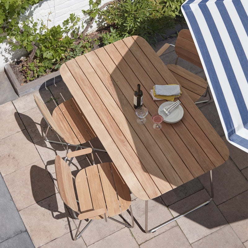 Natural wood dining table with light brown slats, surrounded by beige chairs and a blue and white striped umbrella.