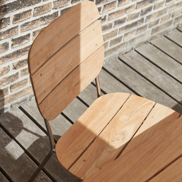 Light wooden chair with a slatted design, showcasing natural grain patterns, set against a textured brick wall.