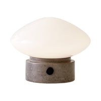 White glass lampshade with smooth curves, set on a textured gray concrete base, accented by a black knob.