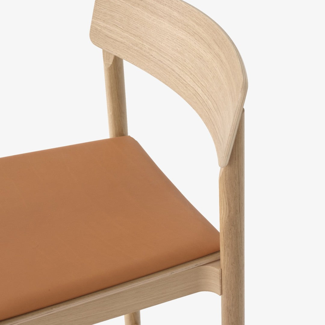 Light wood chair with a smooth tan leather seat, showcasing minimalist design and natural colors.