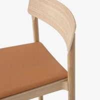 Light wood chair with a smooth tan leather seat, showcasing minimalist design and natural colors.