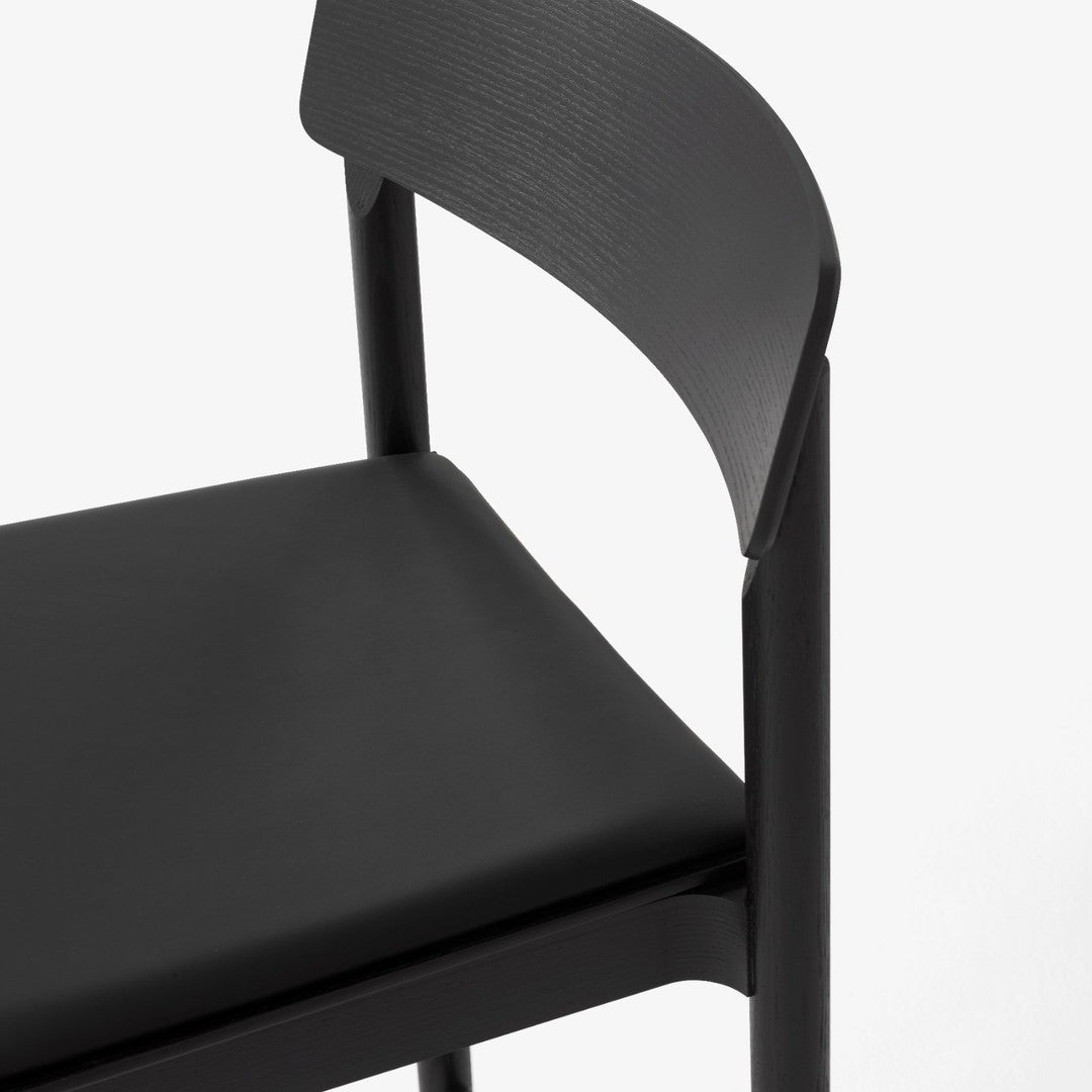Black chair with a smooth, matte finish and minimalist design, featuring subtle wood grain patterns.