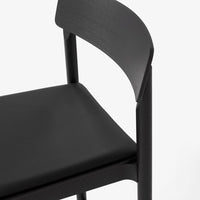 Black chair with a smooth, matte finish and minimalist design, featuring subtle wood grain patterns.