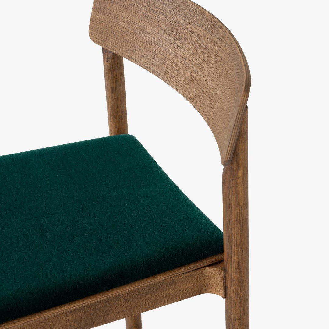 Wooden chair with a warm oak frame and deep green velvet upholstery. Modern design with a soft texture contrast.
