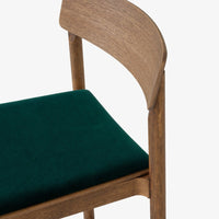 Wooden chair with a warm oak frame and deep green velvet upholstery. Modern design with a soft texture contrast.