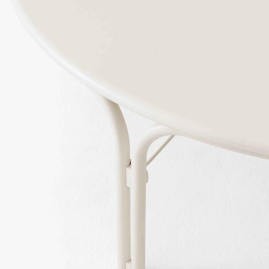 Cream-colored round table with smooth surface and sleek, minimalistic metal legs in a matching hue.