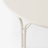 Cream-colored round table with smooth surface and sleek, minimalistic metal legs in a matching hue.
