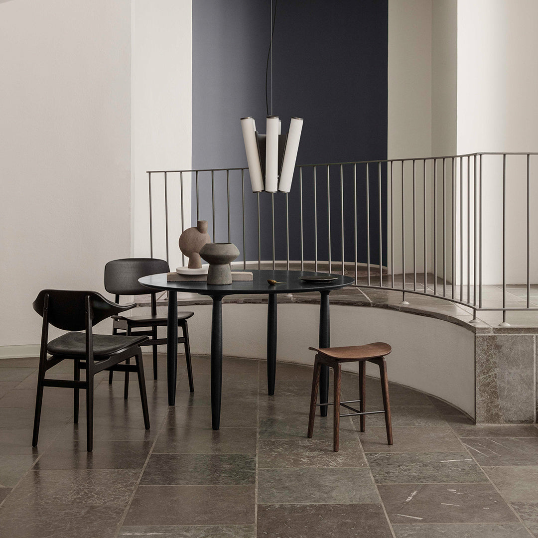 Modern black chairs, circular black table, and natural wood accents against a neutral backdrop with gray stone flooring.