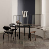 Modern black chairs, circular black table, and natural wood accents against a neutral backdrop with gray stone flooring.