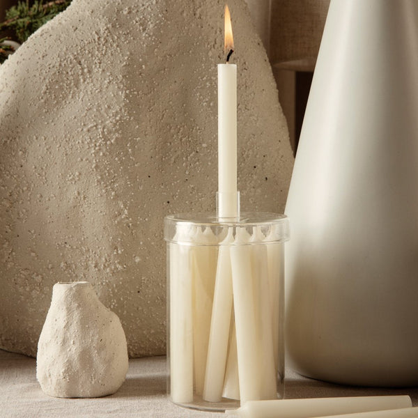 Cream-colored taper candles in a clear holder against neutral backgrounds, featuring soft textures and minimalist design.