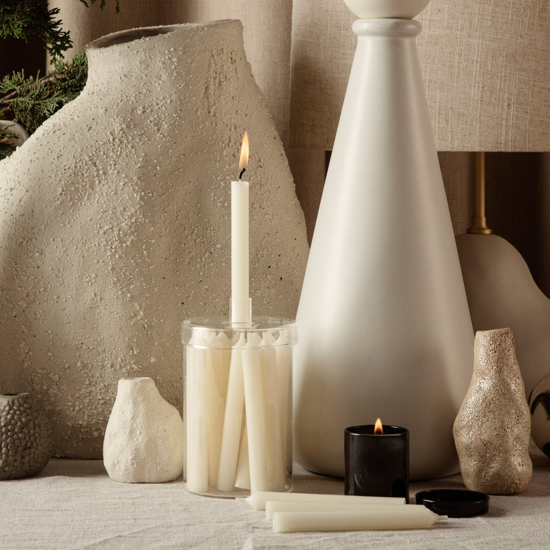 White and black candles with various shapes and textures, set against neutral hues and natural elements.