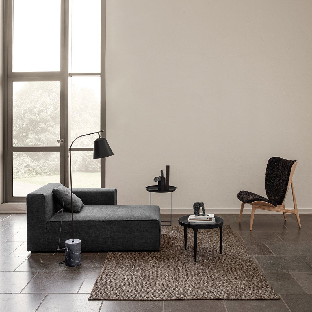 Gray chaise lounge with textured fabric, a dark brown patterned rug, and earthy tones in a minimalist setting.