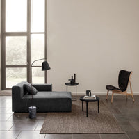 Gray chaise lounge with textured fabric, a dark brown patterned rug, and earthy tones in a minimalist setting.