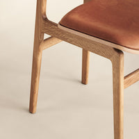 Wooden chair with natural oak finish and rich brown leather seat, showcasing minimalistic design and elegant textures.