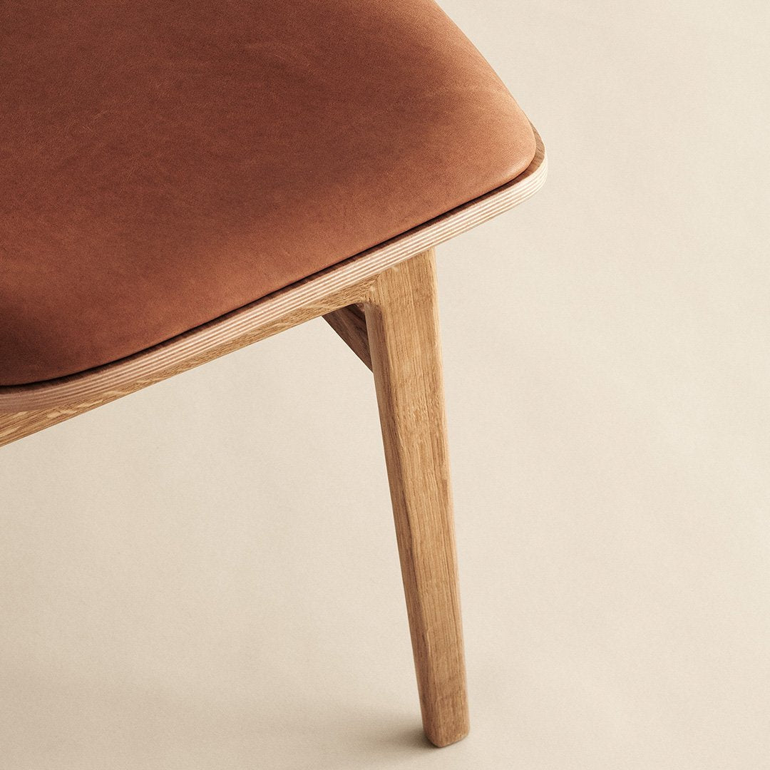 Brown velvet cushion with a smooth finish, paired with light wooden legs. Elegant, minimalist design.