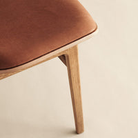 Brown velvet cushion with a smooth finish, paired with light wooden legs. Elegant, minimalist design.