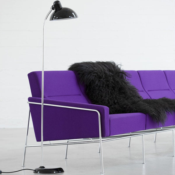 Vibrant purple sofa with smooth fabric and a fluffy black throw, complemented by a sleek black floor lamp.
