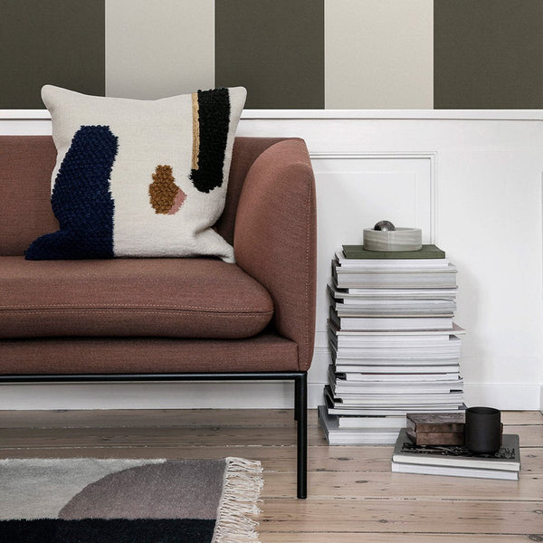 Cream and navy geometric pillow on a brown sofa with black metal frame, accented by neutral wall stripes.