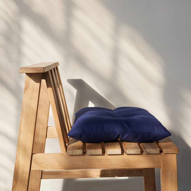 Navy blue cushion on a wooden chair with shadows creating a pattern on the wall. Perfect for indoor or outdoor decor.